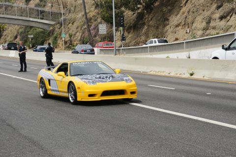 1993 Ford Taurus - A yellow sports car with racing decals drives down a highway, observed by two police officers.