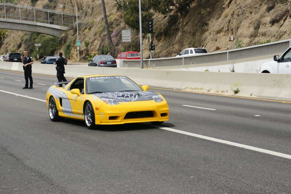 Yellow sports car with 'Gumball 3000' on the hood, driving on a highway with police officers nearby