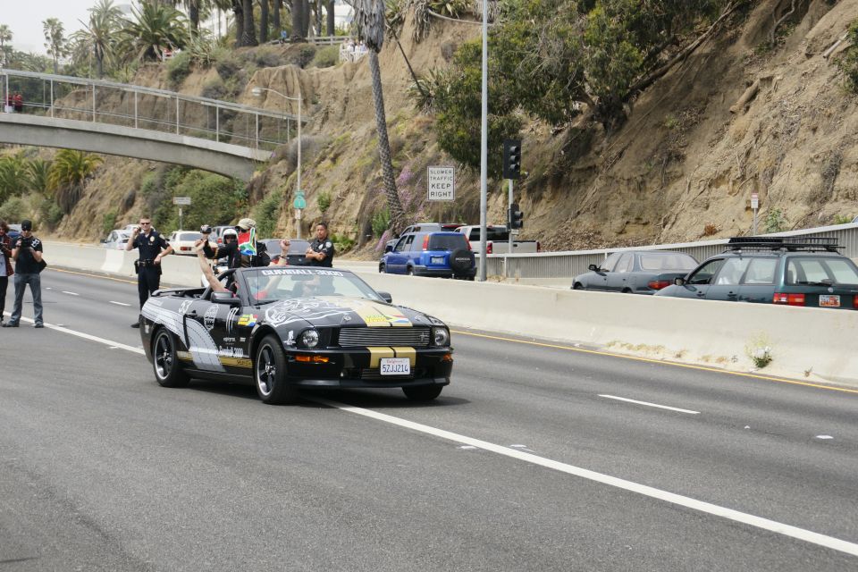 Black convertible Mustang with gold stripes, police escort