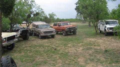 1979 Ford Bronco - Several vehicles, including a red 1978 Ford Bronco, are parked in a grassy, tree-filled area.