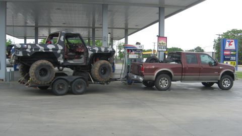 1979 Ford Bronco - Two trucks at a gas station: a Ford Bronco on a trailer and a Ford pickup towing it.