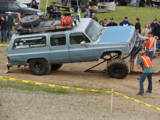 Lifted 1990 Chevrolet Suburban with roof rack, spare tire, and custom front bumper. Photographer is taking a picture