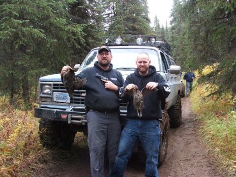 1990 Chevrolet Suburban - Two men display their hunting catch in front of a modified SUV on a muddy forest road.