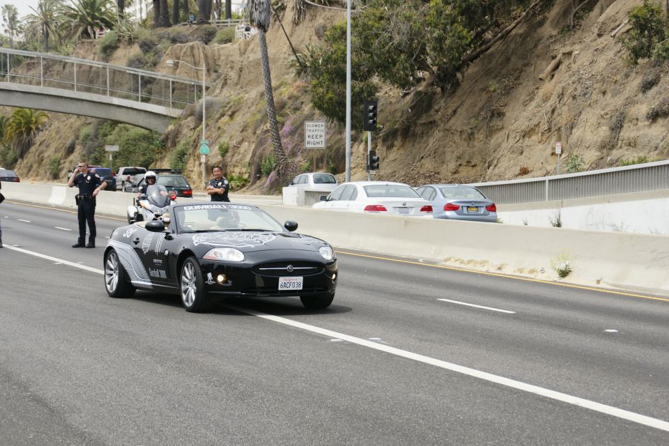Black convertible with police motorcycle escort on highway
