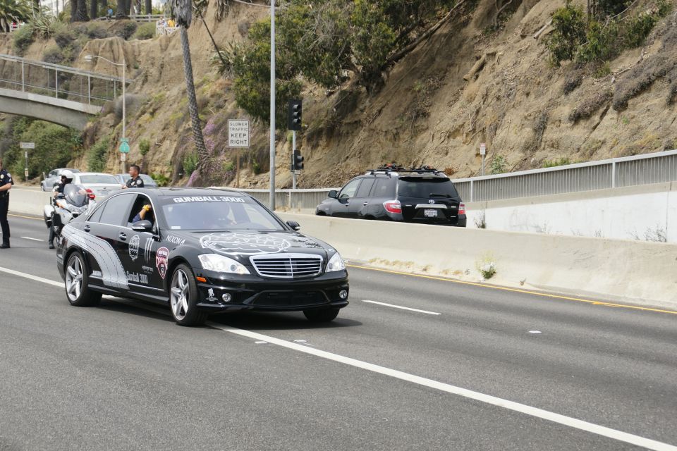 Black Mercedes-Benz S-Class with Gumball 3000 decals driving on highway, black SUV in background