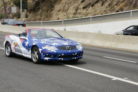 1993 Ford Taurus - A blue convertible with patriotic livery drives on the highway, with other vehicles visible in the background.