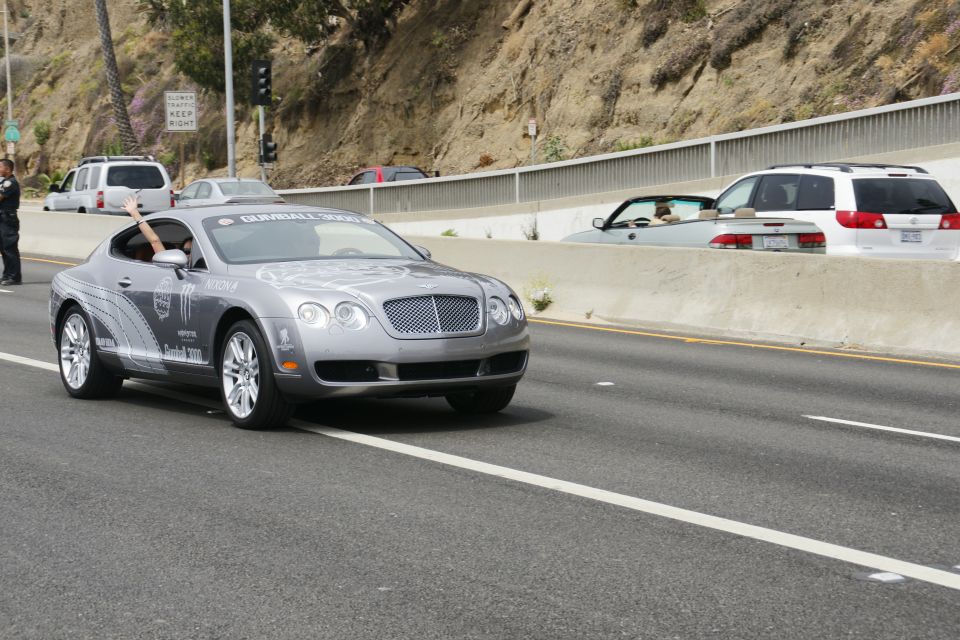 Silver Bentley Continental GT with Gumball 3000 livery driving on highway, other vehicles visible