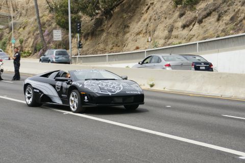 1993 Ford Taurus - A black Lamborghini Gallardo with racing decals is seen on the highway, with a police officer observing.