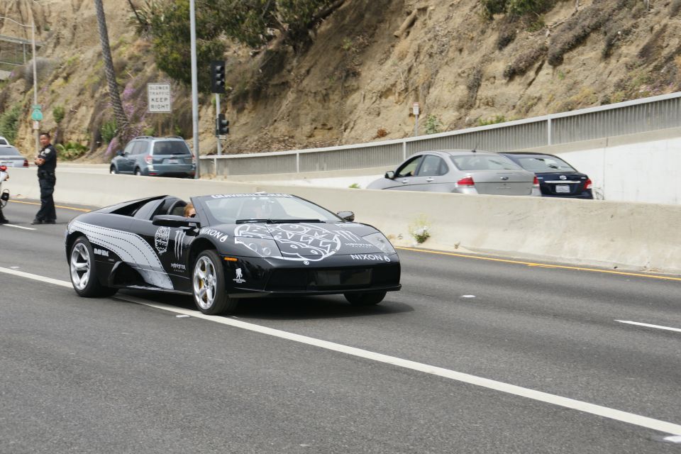 Black Lamborghini Gallardo with Monster Energy and Nixon logos driving on highway. Police officer on left