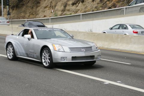 1993 Ford Taurus - A silver Cadillac XLR with Gumball 3000 branding drives on a highway.