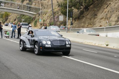 1993 Ford Taurus - A black Bentley Continental GT, adorned with Gumball 3000 graphics and the license plate 144FX, drives on a highway.