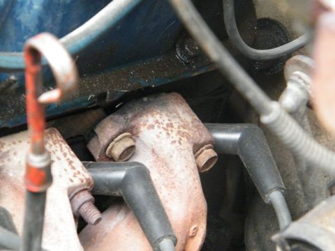 1982 Ford Bronco - Detail of an engine's exhaust manifold and spark plug wires, showing signs of wear and rust.