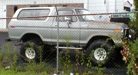 1983 Ford Bronco - This lifted SUV, likely a 1978 model, is seen parked behind a chain-link fence with overgrown vegetation.