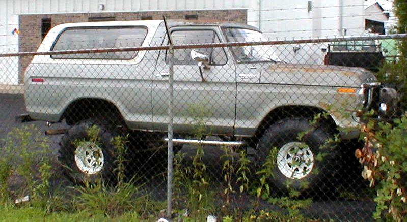 Gray lifted Ford Bronco SUV in side view behind a chain-link fence