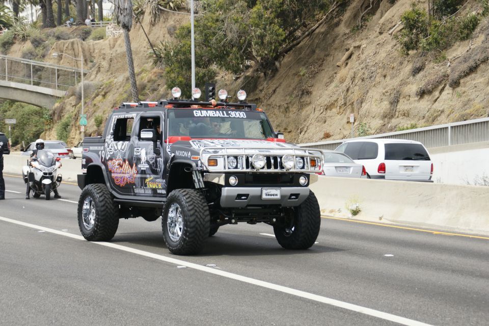 Hummer H2 with Gumball 3000 graphics on highway, police motorcycle nearby