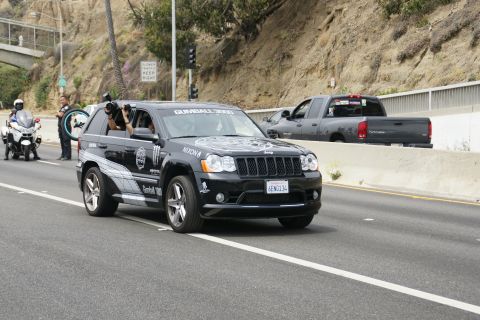 1993 Ford Taurus - A black Jeep Grand Cherokee with Gumball 3000 and Nixon decals drives on the highway, accompanied by police.