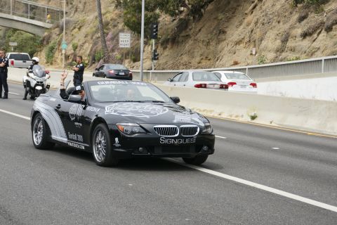 1993 Ford Taurus - A black convertible with Gumball 3000 graphics is seen on the highway, with police officers and a motorcycle nearby.