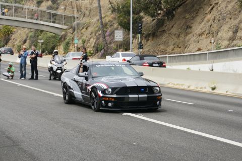 1993 Ford Taurus - A modified black Ford Mustang with shark teeth graphics drives down a highway, accompanied by police officers and a motorcycle.