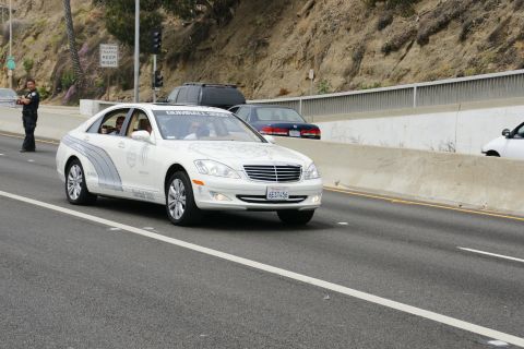 1993 Ford Taurus - A white sedan with Gumball 3000 decals drives on a highway, with other vehicles visible in the background.