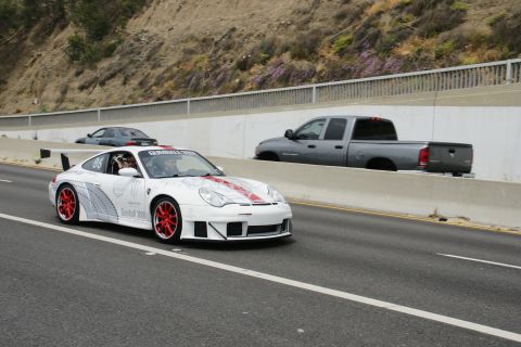 1993 Ford Taurus - Porsche 911 race car with Gumball 3000 decals drives on a highway alongside other vehicles.