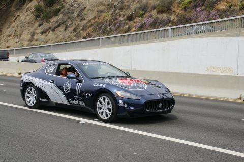 1993 Ford Taurus - A blue Maserati GranTurismo with various sponsor decals, including Monster Energy and Red Bull, drives on a highway.