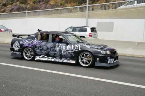 1993 Ford Taurus - A heavily customized sedan with skull graphics drives on the highway, its passenger filming the event.