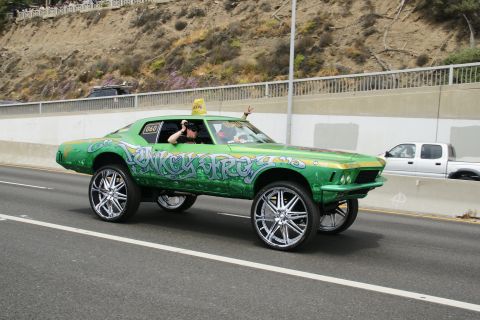 1993 Ford Taurus - Customized green car with graffiti and oversized wheels driving on a highway.