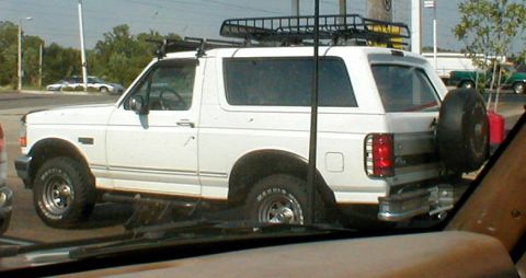 1983 Ford Bronco - This white Ford Bronco is equipped with a roof rack and a spare tire mounted on the rear tailgate.