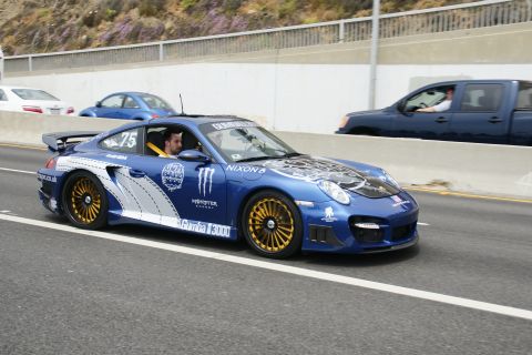 1993 Ford Taurus - A blue Porsche 911, adorned with various racing decals and gold wheels, drives on a highway alongside other vehicles.