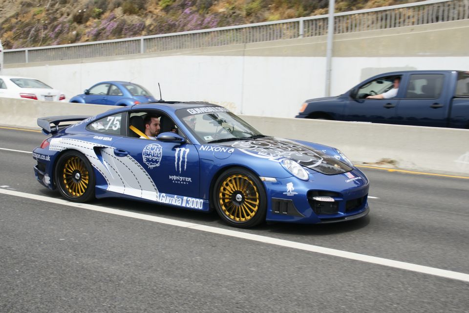 Blue Porsche 911 with Gumball 3000 decals and gold wheels on highway