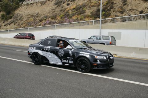 1993 Ford Taurus - Black Audi sedan with Gumball 3000 decals on highway, other vehicles in background.