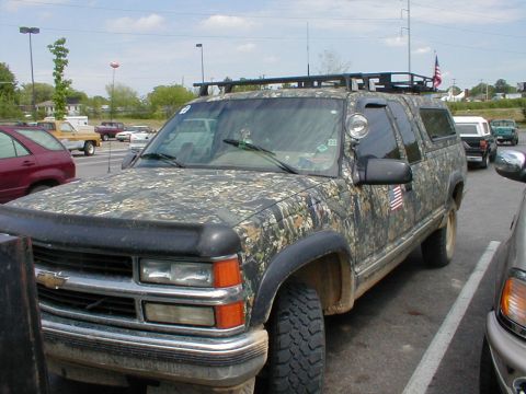 1983 Ford Bronco - This camouflage SUV is equipped with a roof rack and an antenna, suggesting off-road or utility use.