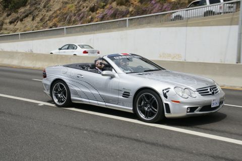1993 Ford Taurus - A silver convertible with racing stripes and a Gumball 3000 sticker drives on the highway, with another car visible in the background.
