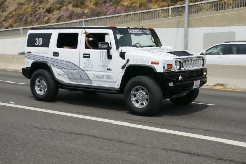 1993 Ford Taurus - White Hummer H2 with Gumball 3000 livery driving on a highway.
