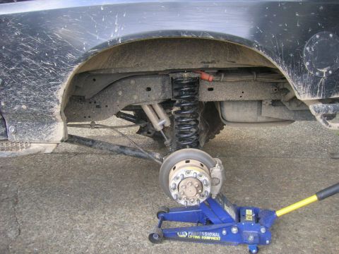 1996 Ford Bronco - Close-up view of the rear suspension system of a vehicle, showing the coil spring, shock absorber, and brake assembly.