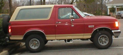 1983 Ford Bronco - This 1983 Ford Bronco is seen from the side, a red body with tan accents and a spare tire mounted on the back.
