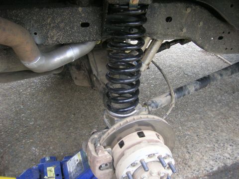 1996 Ford Bronco - The rear suspension and brake components of a vehicle are shown, with a hydraulic jack supporting the frame.