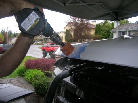 1996 Ford Bronco - A hole saw is used to drill into the hood of a vehicle, with a red SUV visible in the background.