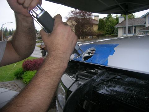 1996 Ford Bronco - A person uses a reciprocating saw to cut a hole in the hood of a vehicle, which is covered in blue tape.