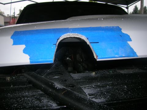 1996 Ford Bronco - A section of a white vehicle fender has been cut out and taped with blue masking tape, revealing the wheel well and suspension components.