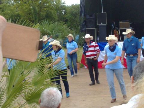 1991 Ford LTD Crown Victoria - A group of people dressed in cowboy attire participate in a line dance at an outdoor festival.
