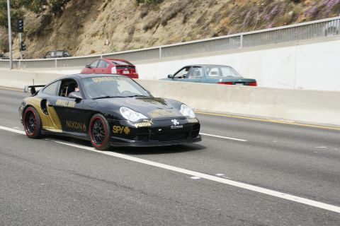 1993 Ford Taurus - A black Porsche 911 with prominent Gumball 3000 branding is captured in motion on a multi-lane road.