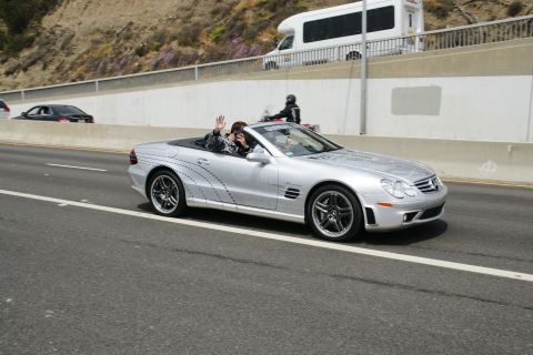 1993 Ford Taurus - A silver convertible sports car with a person waving from the driver's seat drives down a highway.