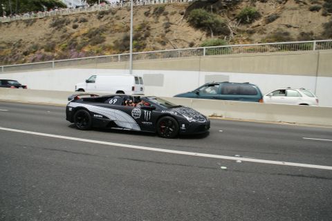 1993 Ford Taurus - A black convertible sports car with numerous racing decals, including the number 69, drives on a highway.