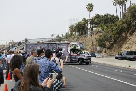 1993 Ford Taurus - A crowd watches a custom RV with a large eye graphic pass by on a highway.