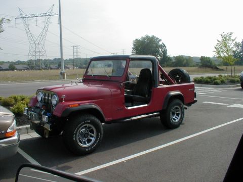 1983 Ford Bronco - A red Jeep CJ-7 is parked in a lot, showing its side and front quarter view.
