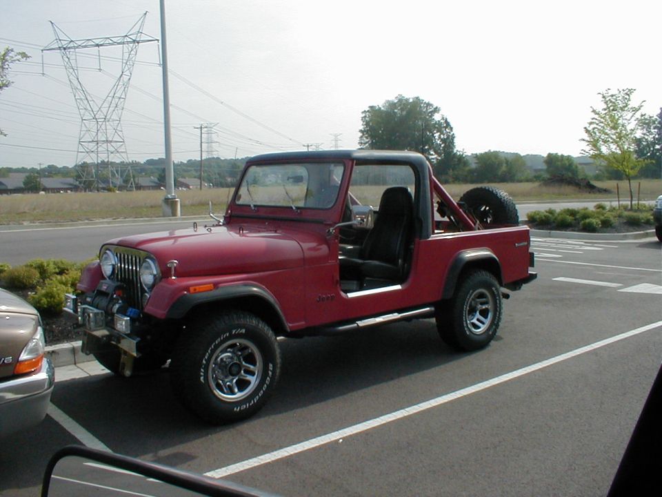 Red topless Jeep CJ Scrambler with winch and chrome wheels in a parking lot