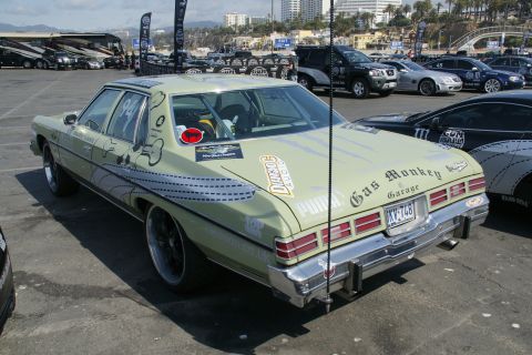 1993 Ford Taurus - A vintage sedan with racing decals is parked at an outdoor event with other vehicles and buildings in the background.