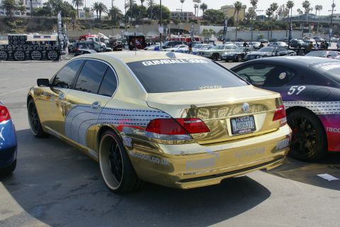 1993 Ford Taurus - A gold-wrapped BMW 7 Series sedan is parked at an outdoor event, with other vehicles visible in the background.