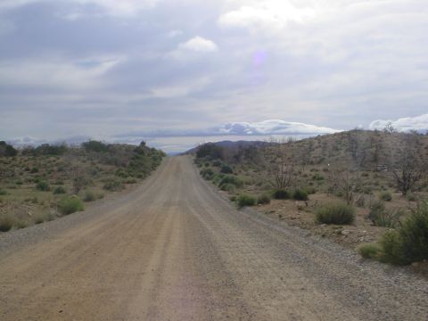 1994 Ford Bronco - A long dirt road stretches through a barren desert landscape under a cloudy sky.